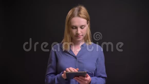 年轻的金发白种人妇女与平板电脑合作的肖像并显示其显示在相机的黑色背景视频的预览图