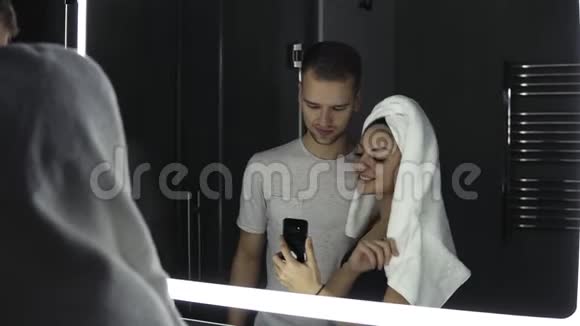浴室里的男人和女人在镜子里拍照头上戴白色浴巾的女人黑暗视频的预览图