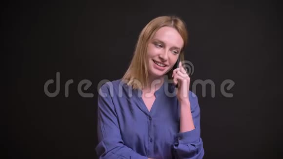 白种人金发女子穿着衬衫在黑色背景下用心地用手机说话视频的预览图
