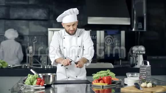 男厨师在专业厨房摆姿势厨师玩磨刀视频的预览图