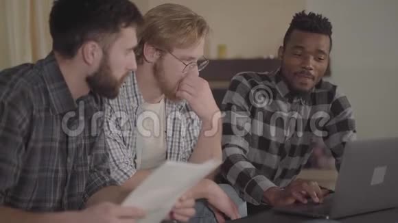 两个高加索人和一个非裔美国人在家休息坐在笔记本电脑前多元文化视频的预览图