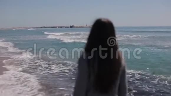 在海滩上一个长着一头松松的黑发的女孩在水中行走慢动作视频的预览图