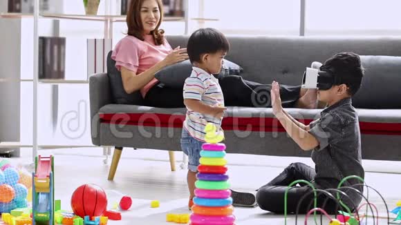 亚洲妈妈坐在沙发上大儿子用虚拟现实和弟弟在客厅视频的预览图
