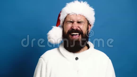 戴着顶帽子的大胡子男人在蓝色的背景上真诚地微笑蓝色背景的搞笑圣诞老人概念视频的预览图