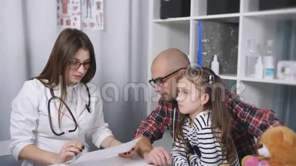 一位女医生检查了一个喉咙痛的小病人在儿科医生的招待会上父亲和女儿视频的预览图