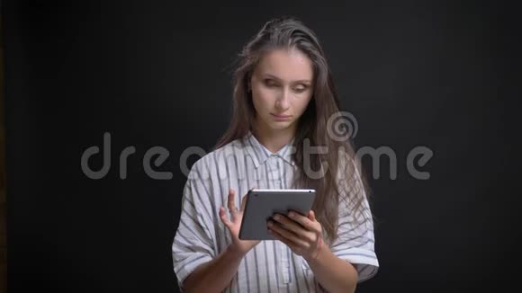 一幅美丽的白种人长发女人的肖像她在黑色背景下体贴地用平板电脑工作视频的预览图