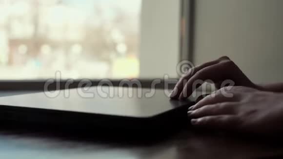 女人的手缓慢地打开靠近窗户的笔记本电脑特写的盖子视频的预览图