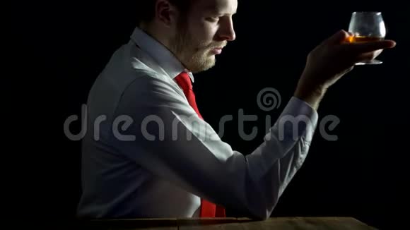 一个穿着白色衬衫带着胡须的领带的男人看着一杯酒想着黑色的背景脱色视频的预览图