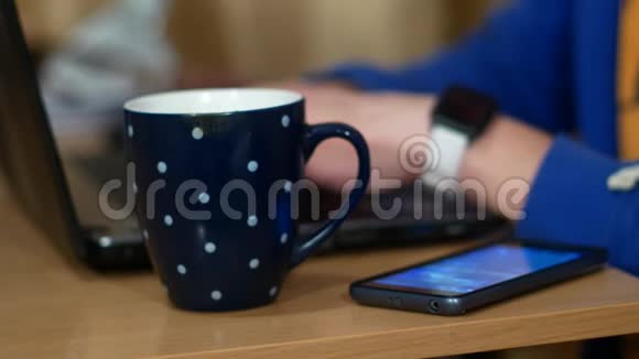 自由职业者正在做笔记本电脑在一杯热饮料旁边一个人喝茶脱下智能手表视频的预览图