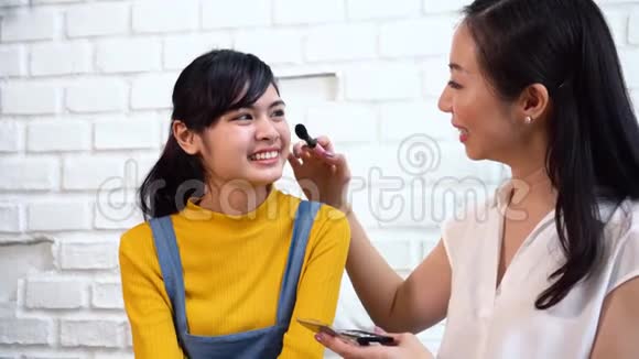 积极的亚洲妈妈在沙发上给女儿化妆视频的预览图
