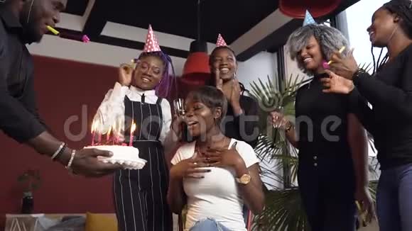 情绪激动的非洲女孩在生日聚会上吹蜡烛在生日蛋糕上包围了她的朋友视频的预览图
