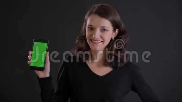 年轻的白种人长发女孩的肖像微笑地显示绿色的智能手机屏幕在黑色背景下拍摄视频的预览图