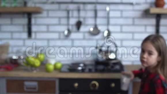 可爱的小女孩穿着格子衬衫拿着一个杯子坐在厨房的桌子旁视频的预览图