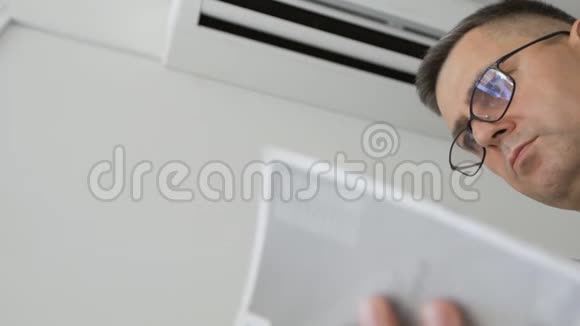 一个戴眼镜的人站在一台工作空调旁边正在学习该装置的说明书视频的预览图