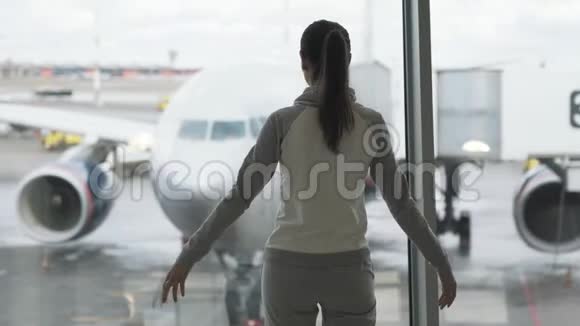 从侧面看女孩站在机场窗前背景是飞机举起双臂表达自由视频的预览图