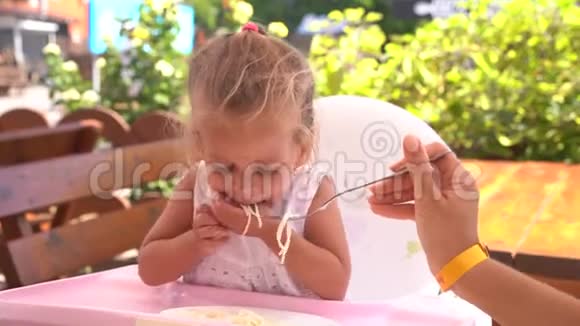 可爱的白人小女孩坐在儿童座椅户外餐厅的桌子上吃意大利面视频的预览图