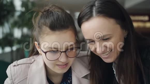 小女儿和妈妈在咖啡馆里消遣妈妈和十几岁的女儿一起看智能手机上的照片玩得开心视频的预览图