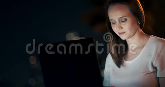 年轻女子夏夜坐在草地上手提电脑在城里视频的预览图