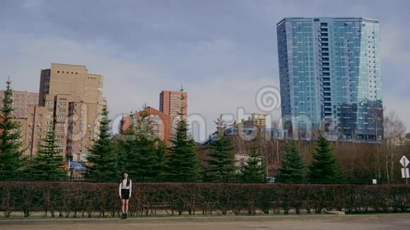 女孩看着摩天大楼和森林背景上的相机少年在脚上荡秋千视频的预览图