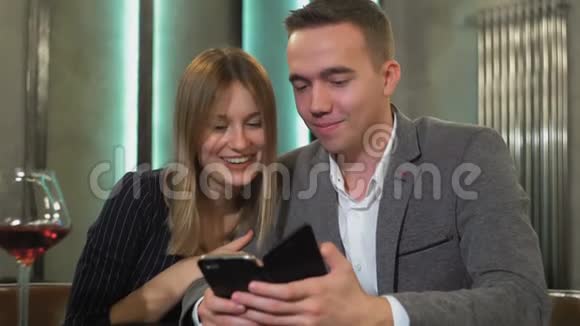 一对年轻漂亮的夫妇在咖啡馆里约会在智能手机上看照片视频的预览图