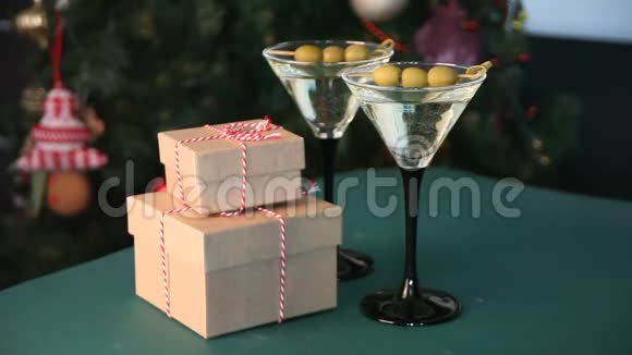 绿色桌子上有两杯马提尼和橄榄和礼品盒浅花圈和圣诞树上面有树视频的预览图