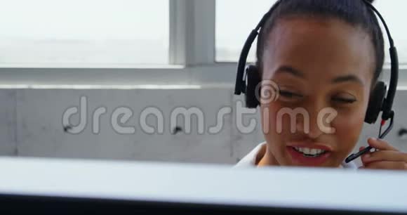 非洲裔美国女商人在现代化办公室的办公桌前用耳机交谈的前景视频的预览图