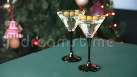 绿色桌子上有两杯马提尼和橄榄和礼品盒浅花圈和圣诞树上面有树视频的预览图