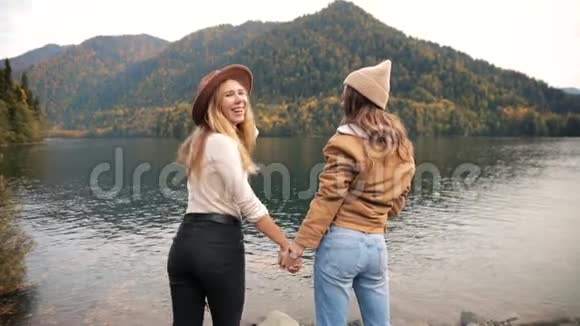 两位迷人的年轻姑娘穿着时髦的衣服在山上的一个湖上度假看着令人惊叹的景色视频的预览图