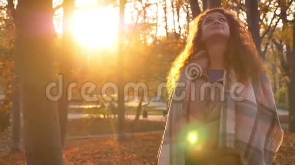 年轻的白种人卷发女子的肖像在闪闪发光的秋天公园背景下兴高采烈地观看着镜头视频的预览图