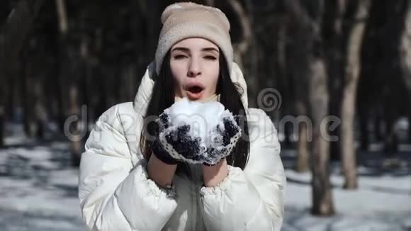 一个黑发女孩穿着白色羽绒服戴着冬手套手里拿着雪吹着雪视频的预览图
