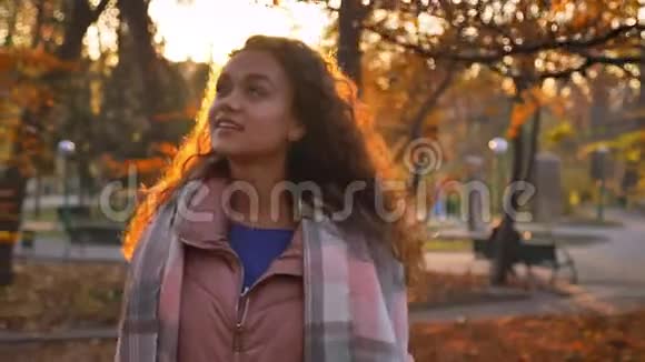年轻的白种人卷发女人拿着棍子在阳光明媚的秋天公园里快乐地散步的肖像视频的预览图