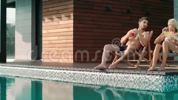 快乐的一对夫妇在豪华住宅游泳池附近的太阳椅上放松视频的预览图
