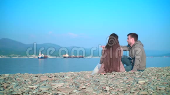 一个年轻的女孩和一个男人在春天的海滩上坐着说话那个女孩和那个相框里的家伙旋转视频的预览图
