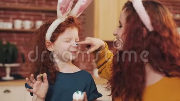 复活节快乐年轻的母亲和她的小女儿互相画鸡蛋和脸家庭笑话视频的预览图
