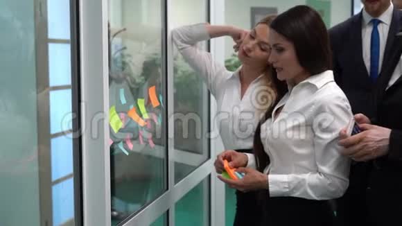 布鲁内特女商人向同事透露玻璃上的彩色纸条视频的预览图
