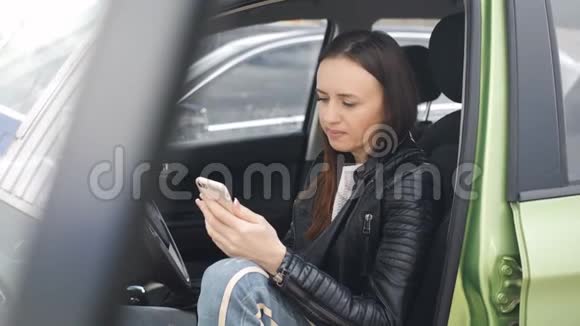 一位女士坐在停车场的一辆车的方向盘后面车门开着用的是智能手机视频的预览图