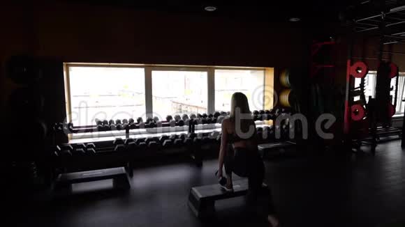 年轻的健身女子手里拿着哑铃蹲健身房里的场景穿着哑铃运动服的女人慢慢视频的预览图