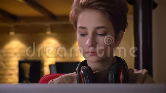 特写肖像年轻的短发女人戴上耳机稍微移动到音乐坐在办公室视频的预览图