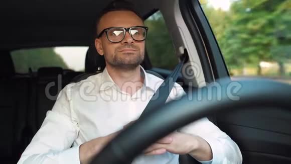 在阳光明媚的天气里戴着眼镜穿着白色衬衫的胡子男驾驶汽车视频的预览图