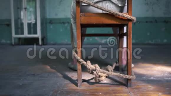 一个疯子坐在破旧的房间里被绑在一张旧蓝椅子上视频的预览图