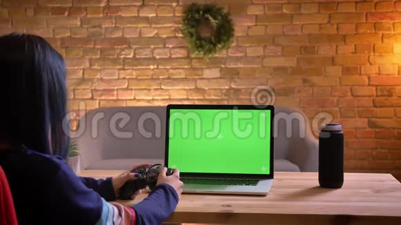 年轻漂亮的女视频博主在笔记本电脑上使用绿色控制台玩视频游戏的特写镜头视频的预览图