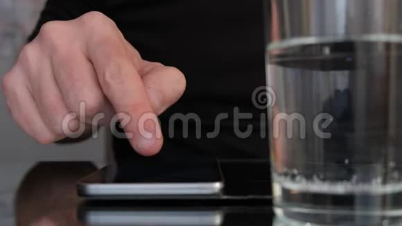 男人手在智能手机上滚动桌子上有一杯水慢动作视频的预览图