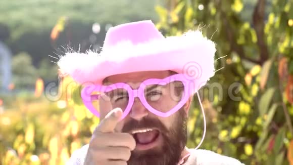 情感男人带着滑稽的时髦粉色太阳镜和滑稽的粉红色帽子胡子疯男人看着镜头开玩笑视频的预览图