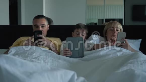 一个幸福的家庭家人父母和儿子躺在床上看视频和亲朋好友聊天视频的预览图