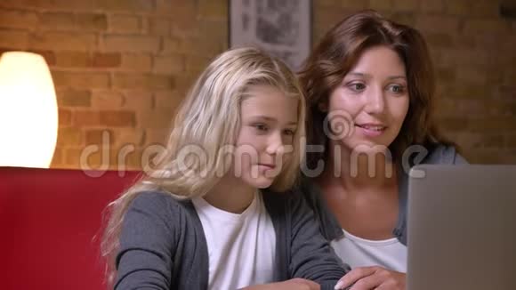 年轻母亲和女儿在笔记本电脑上看电影并愉快交谈的特写镜头视频的预览图