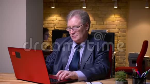 戴眼镜穿着正式服装手提电脑在办公室专心工作的老人的肖像视频的预览图