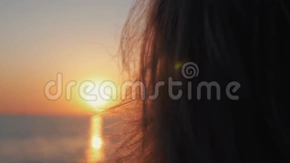 一位年轻女子在海上日落的背景下触摸阳光的手夕阳的金色太阳视频的预览图