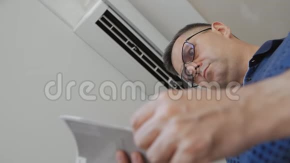 一个戴眼镜的人站在一台工作空调旁边正在学习该装置的说明书视频的预览图