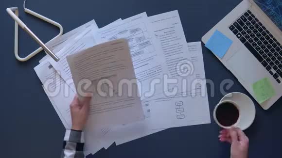一个穿灰色衬衫的女商人在桌旁讨论工作文件喝咖啡桌子上有一台笔记本电脑视频的预览图