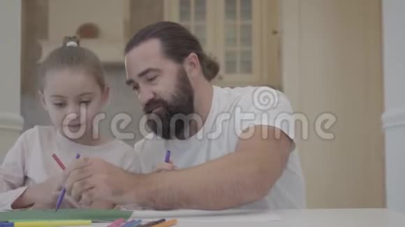 长胡子的男人和小女孩在家里坐在桌子旁用记号笔画画父亲帮助女儿画画支持视频的预览图